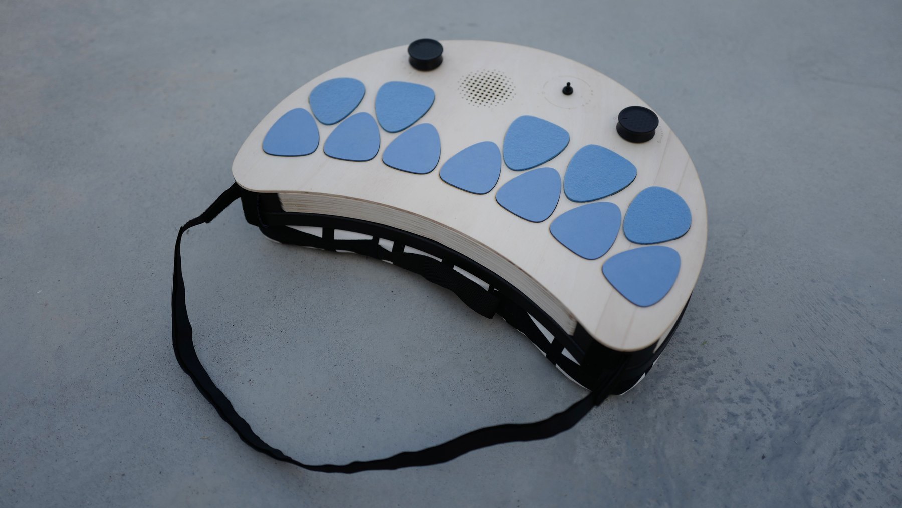 Davido: a curved plywood instrument with fourteen large blue keys, two knobs and a shoulder strap